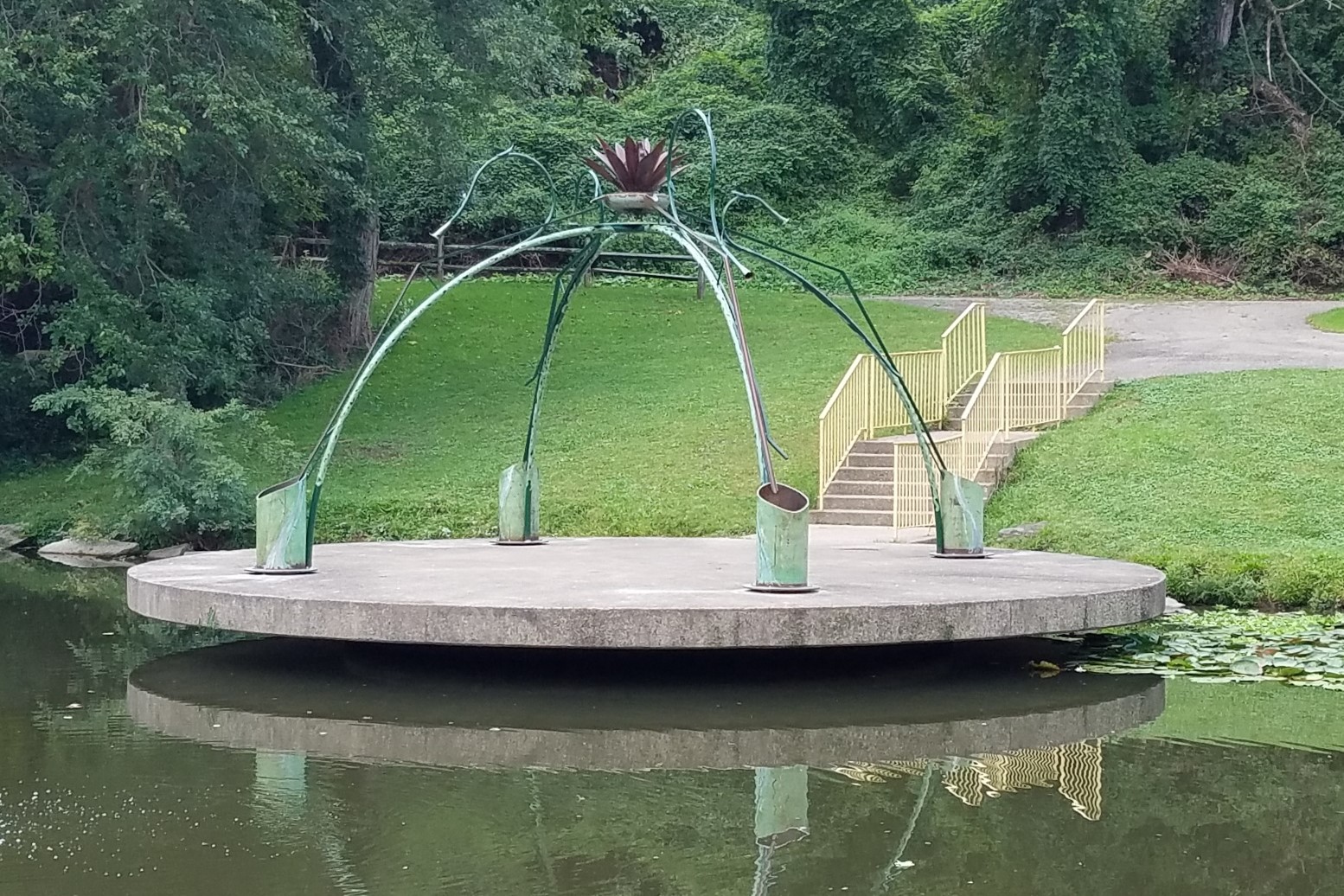 Large piece of public art on a cement circle over a pond in Highland Park.