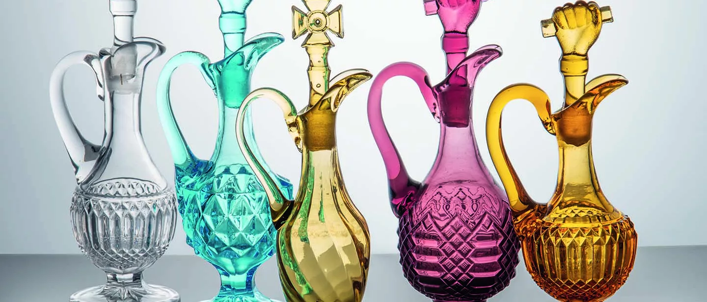 FIve colorful glass jugs are shown -- clear, turquoise, yellow, pink and orange