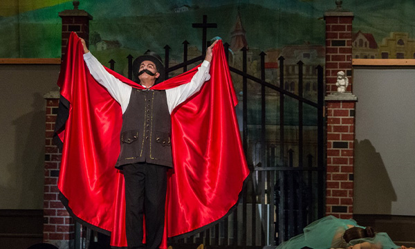 Musical performer - a man on stage with a red cape and a large mustache