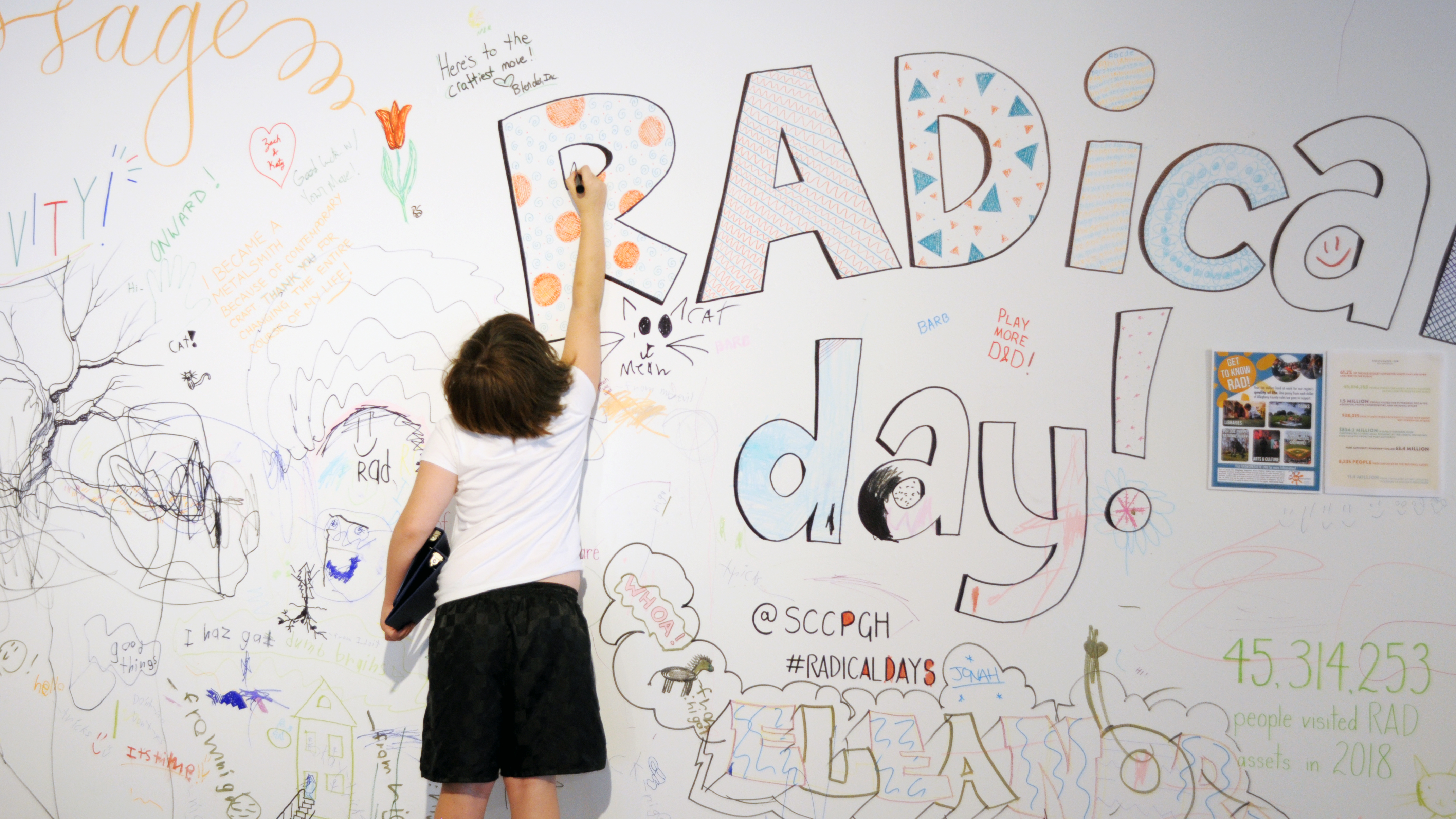 Child writes on a wall covered in art at Contemporary Craft