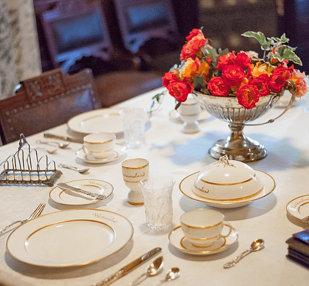 Fancy table place setting with red flowers in a vase.