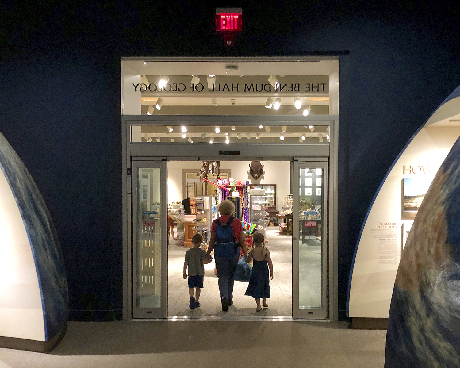 Woman holding hands with two children, walking through automatic doors at the Carnegie Museum of Natural History.