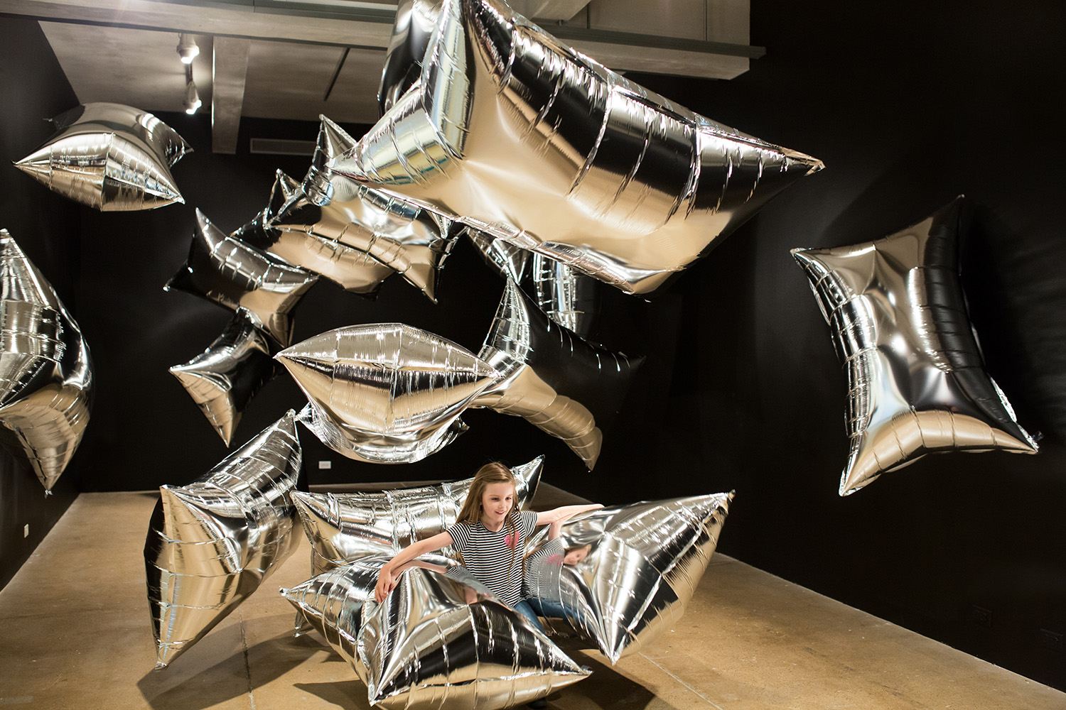 Little girl sitting among huge silver balloons.