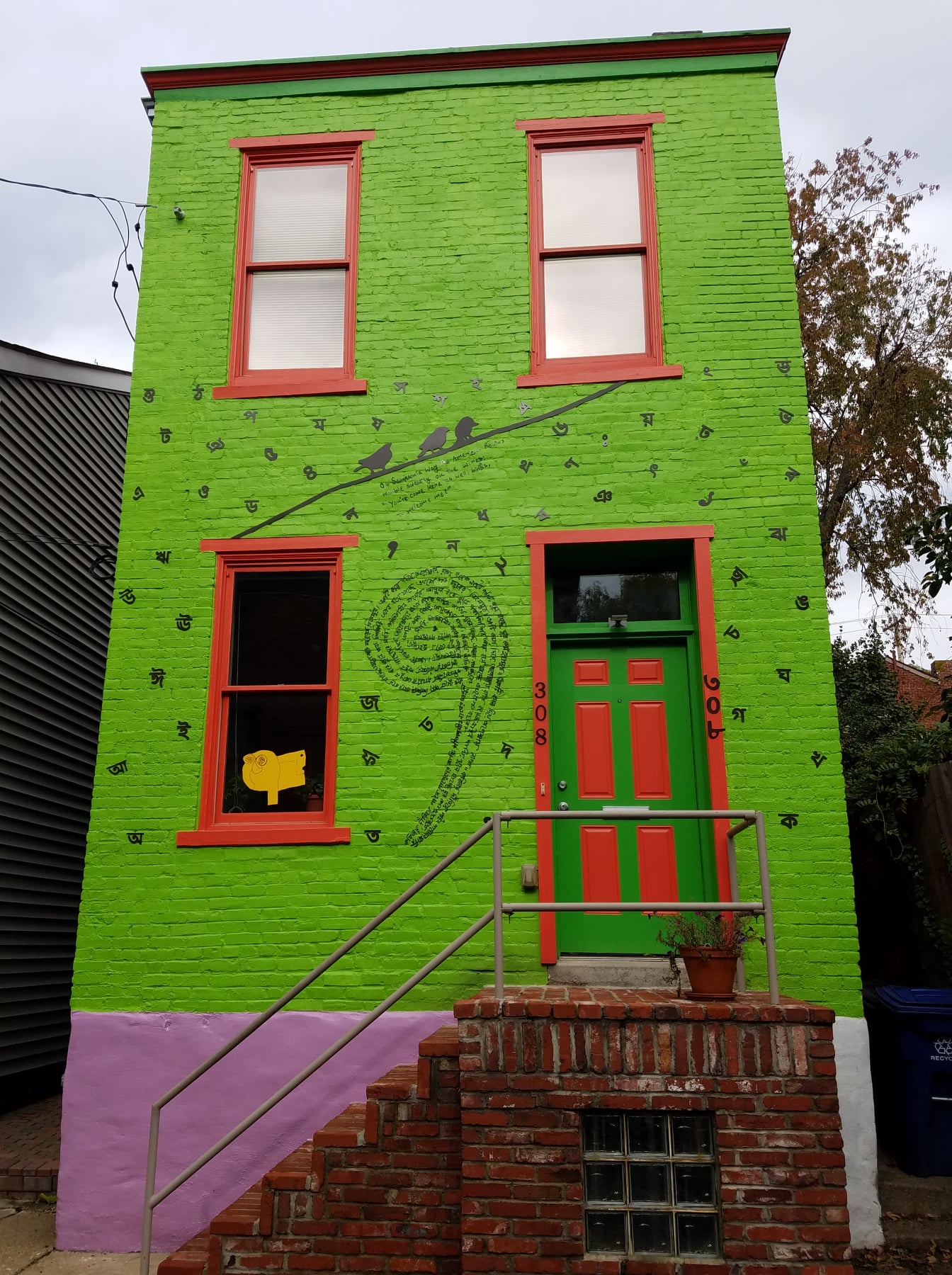 Exterior of a bright green house with red trim and black painted words, characters, and drawings.