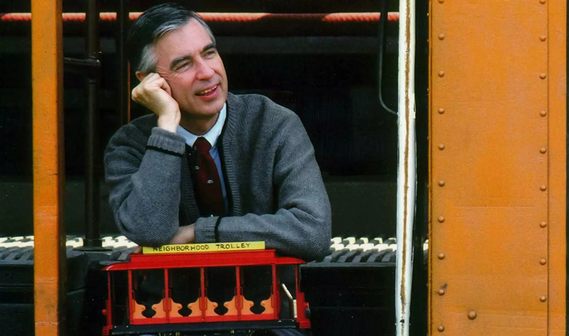 Vintage photo of Fred Rogers sitting on a school bus step with a toy trolley