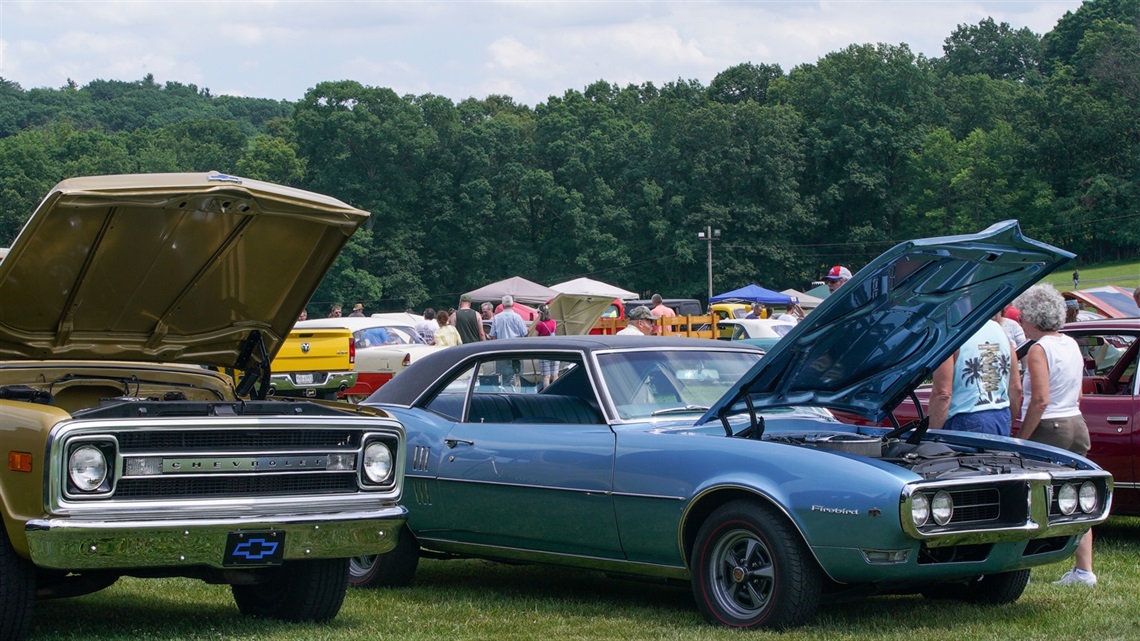 Photograph of people walking among classic cars with their hoods up