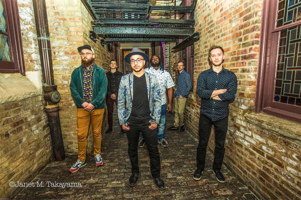 Photograph of the band standing in a hallway, a mix of men of different races