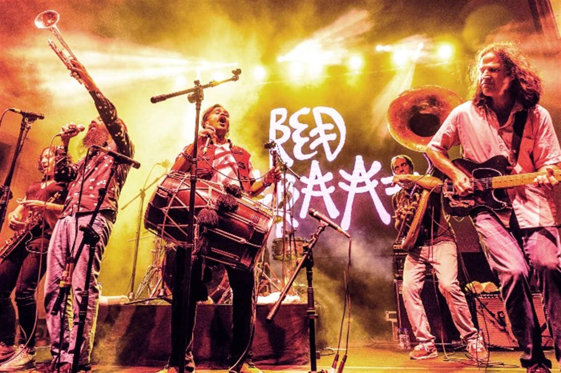 On-stage photo of Red Baraat, with the band playing brass instruments, guitar and a giant drum
