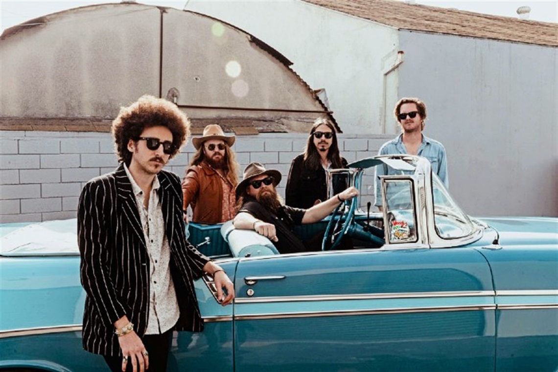 Five members of Robert Jon & The Wreck posing in sunglasses, standing in and around a classic car