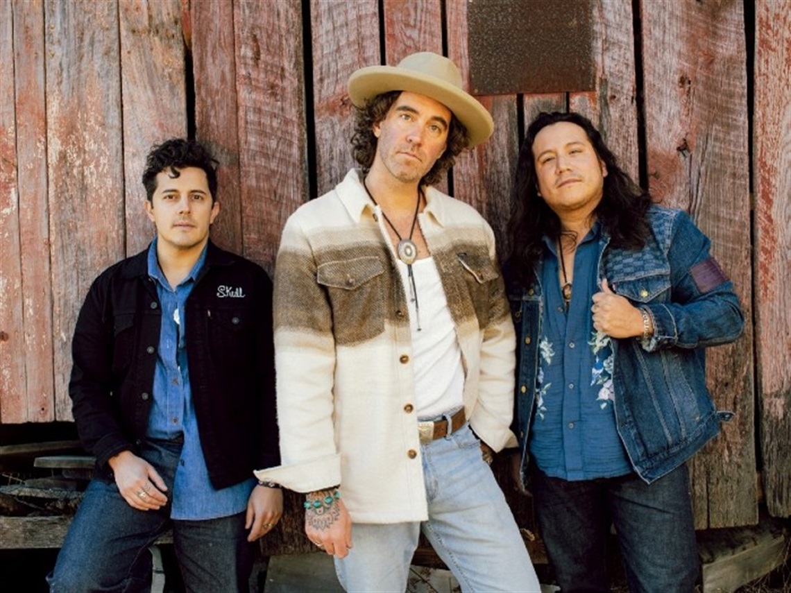 Three members of American Authors, dressed in denim, posing in front of a red barn