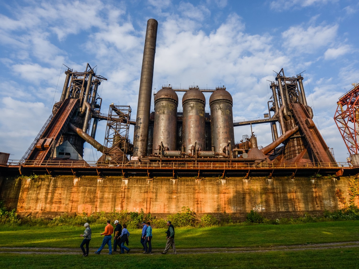 Photo of a group of seven people walking in front of a giant industrial steelmaking furnace