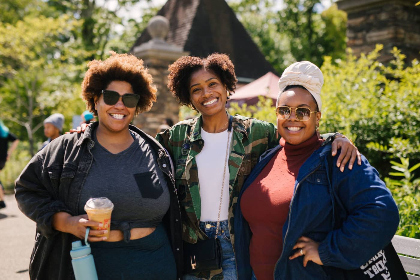 Three women smiling at a camera outside the Frick Environmental Center, a leafy setting
