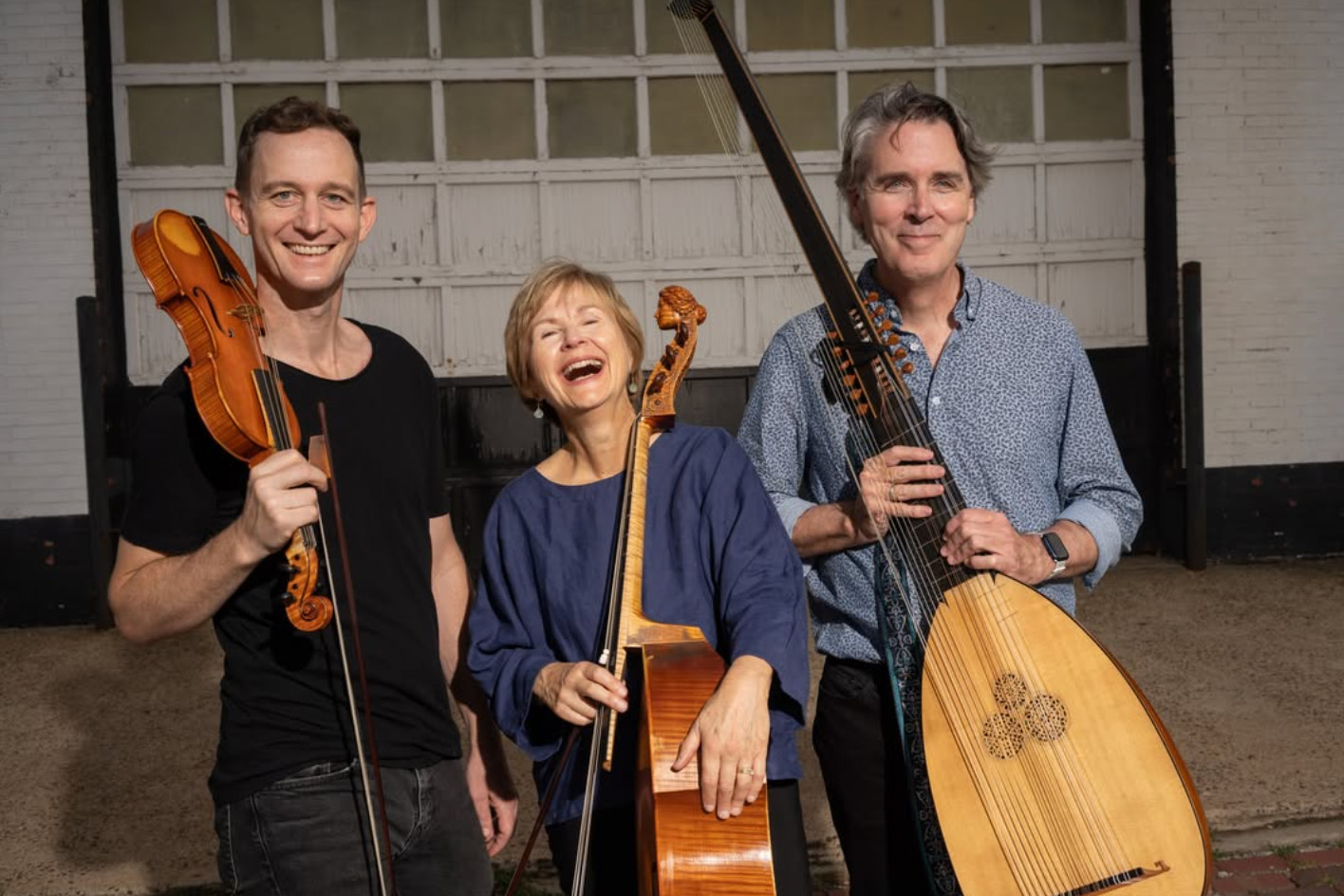 A trio of musicians standing and smiling with their instruments