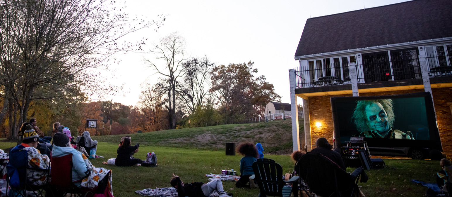 Photo of people sitting on a lawn behind a visitors center watching Beetlejuice, Beetlejuice