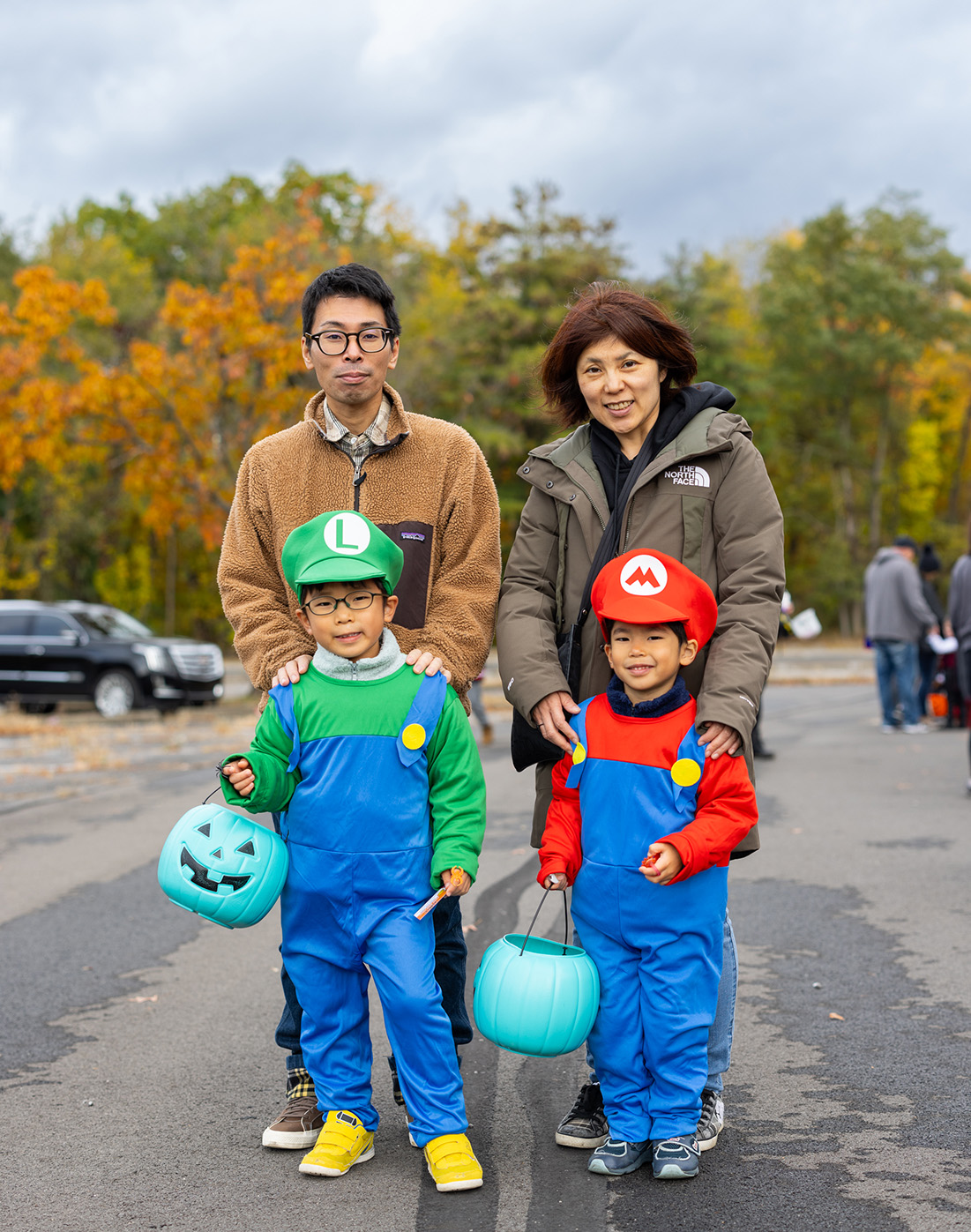 Family dressed up for Halloween standing in front of trees, with the children dressed like Mario and Luigi